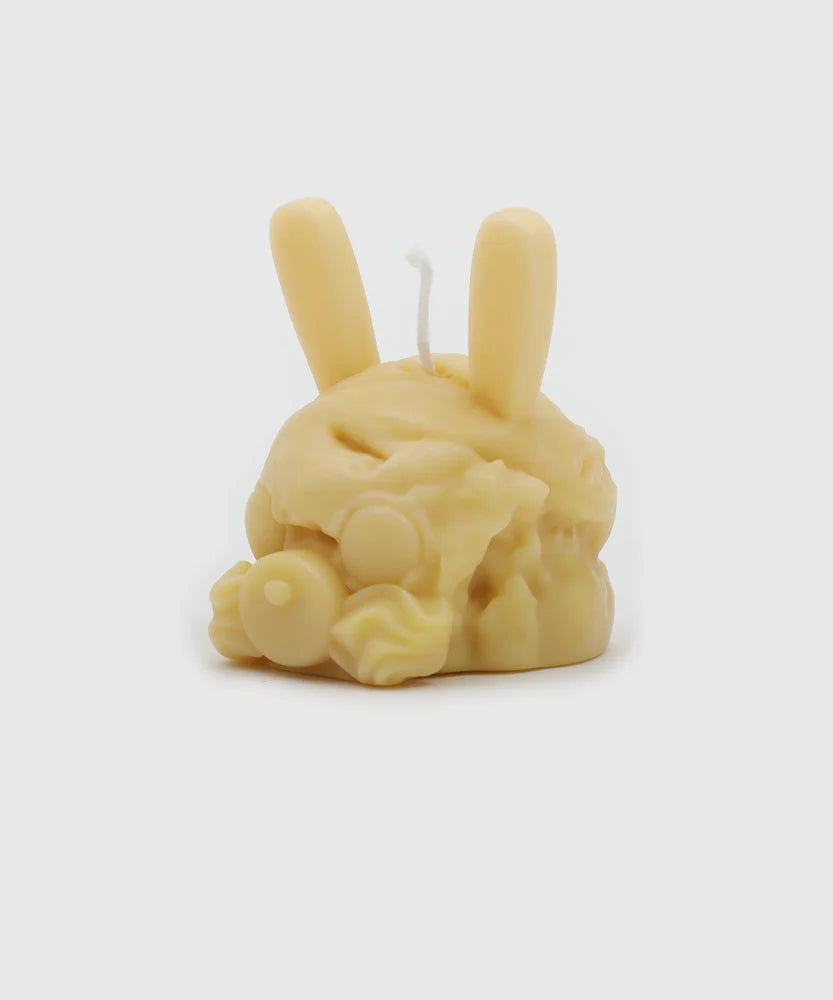 Side view of a light yellow bunny-shaped candle with sculpted frosting-like texture, pacifier nose, and long upright ears – part of the Sucux Cool Collection.
