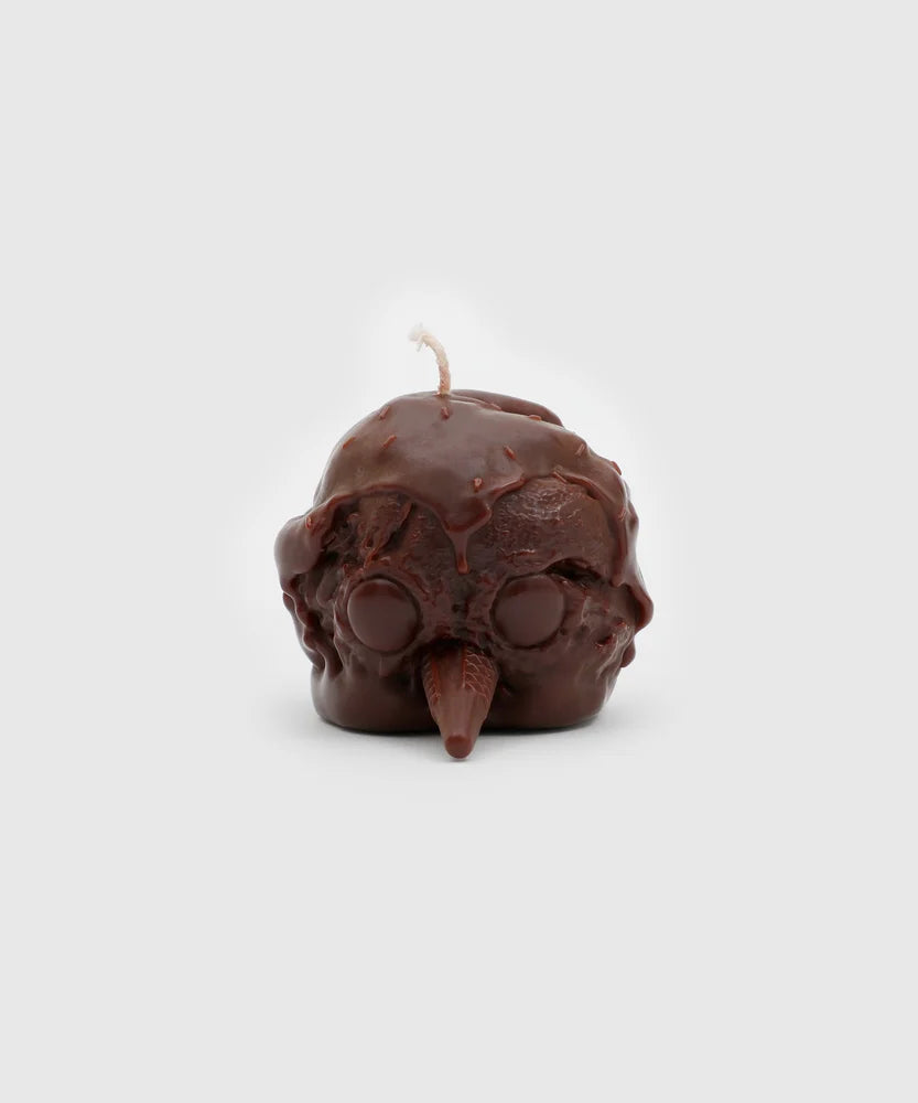 Front view of a chocolate-brown candle shaped like a penguin head, with a textured ice cream scoop surface, round closed eyes, cone-shaped beak, and dripping glaze detail – part of the Sucux Cool Collection.