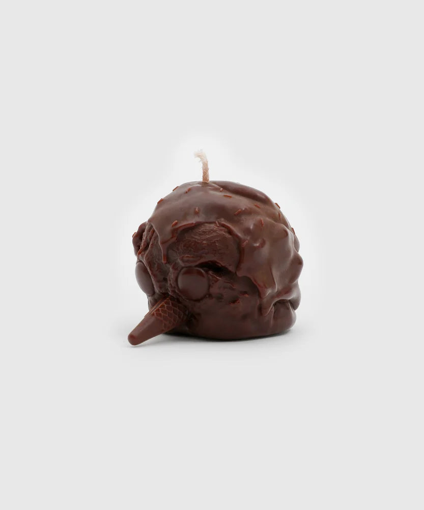Angled side view of a chocolate-brown penguin-shaped candle with a melting scoop texture, round eyes, and an ice cream cone beak – part of the Sucux Cool Collection.