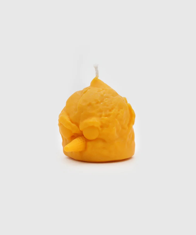 Angled side view of a bright yellow candle shaped like a bird head with closed eyes, textured scoop surface, and cone-shaped beak – part of the Sucux Cool Collection.