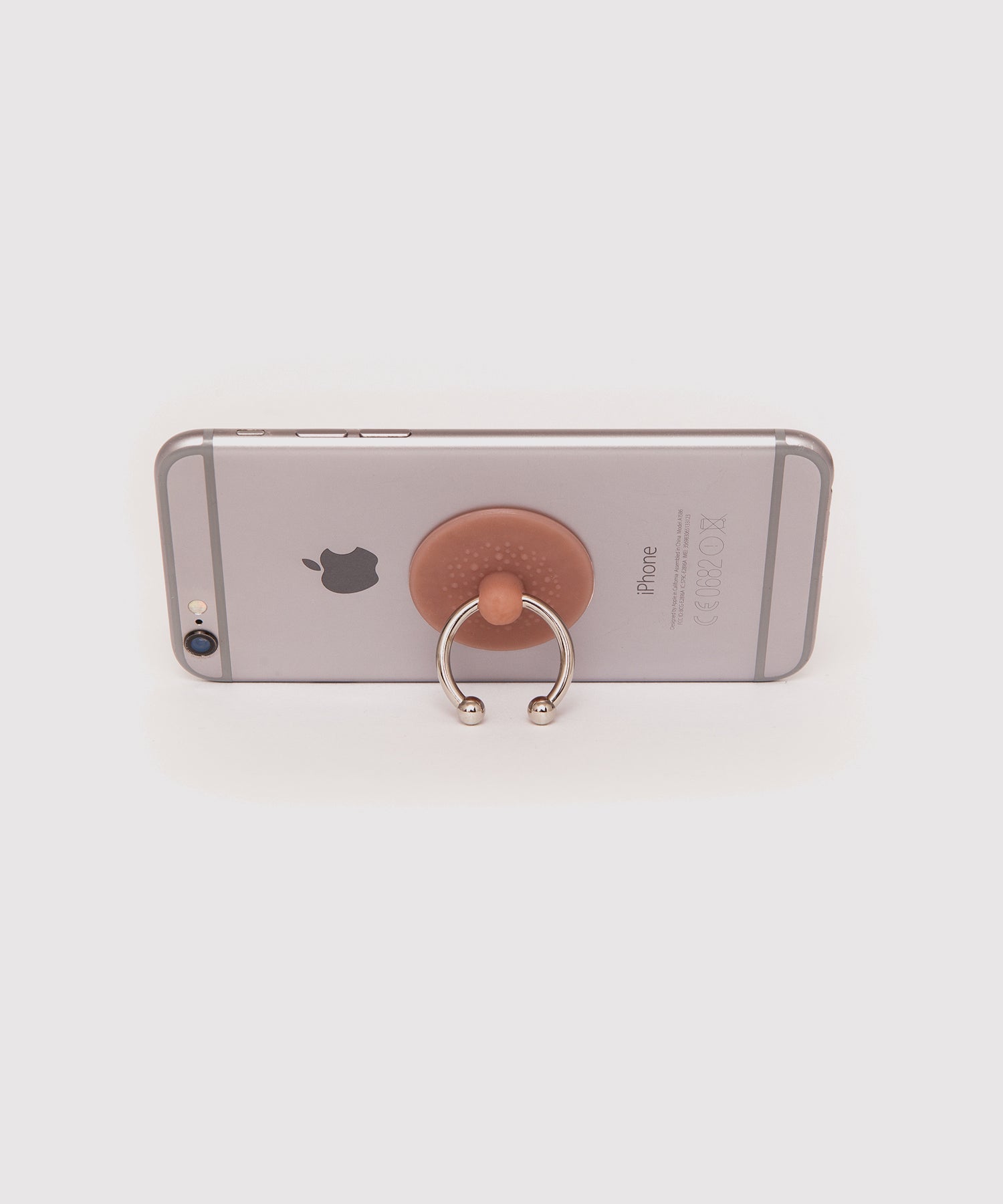 Silver iPhone placed horizontally, supported by a nipple-shaped phone ring holder. The holder functions as a stand, with the metal ring keeping the phone upright.