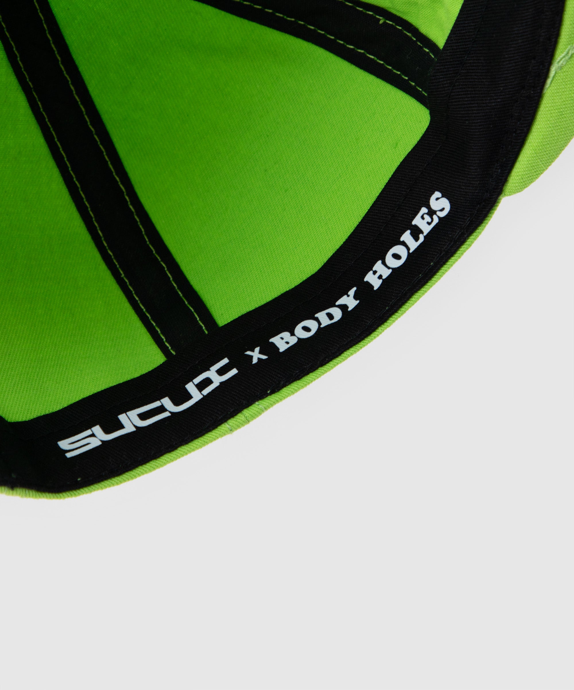 Close-up of the inner seam of a lime green cap, showing the ‘SUCUX x BODY HOLES’ collaboration branding printed on the sweatband – detail from the Alien Head Cap.