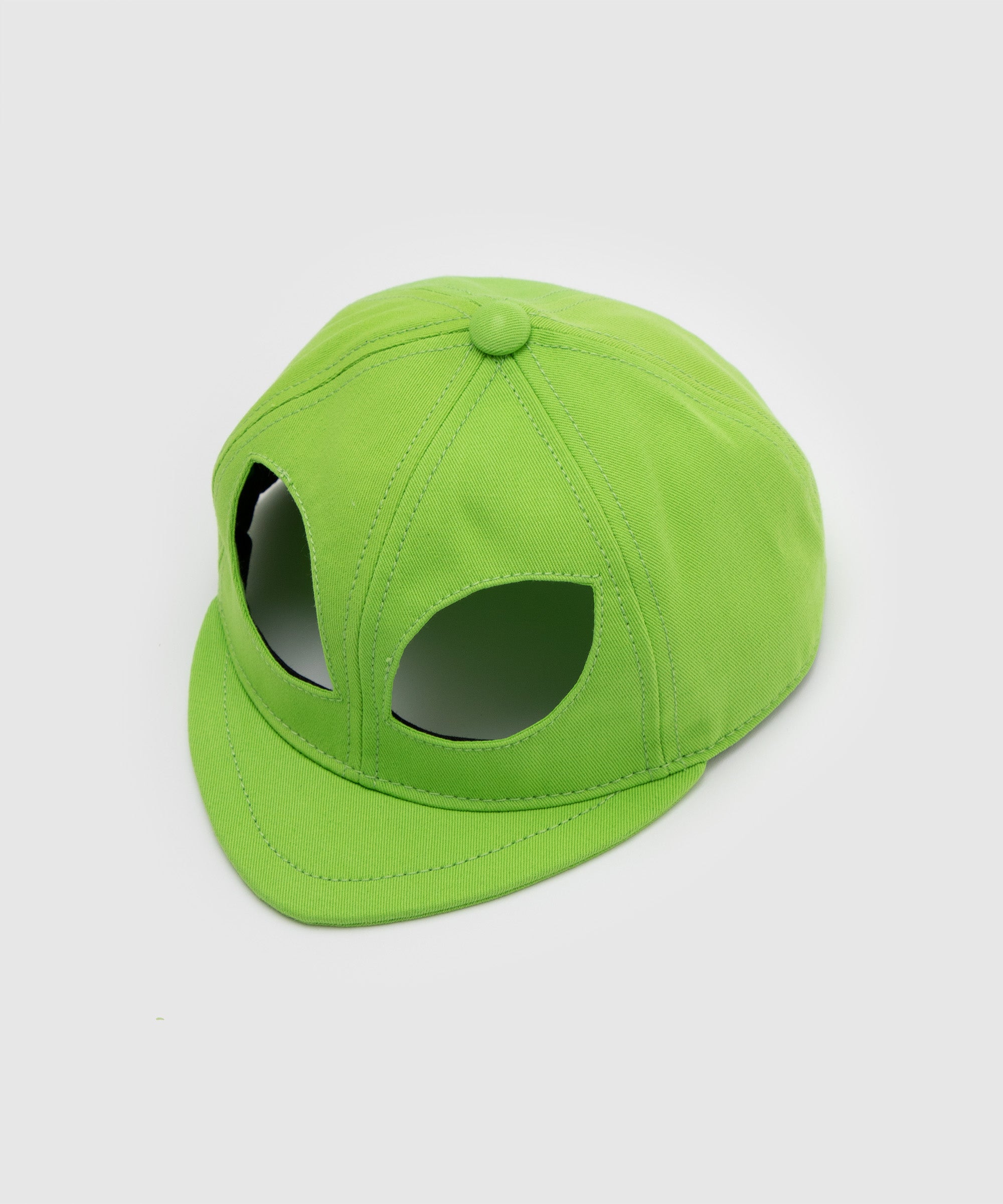 Side angle view of a lime green cap featuring large cut-out eye shapes, mimicking an alien head design – conceptual accessory by Sucux Lab.