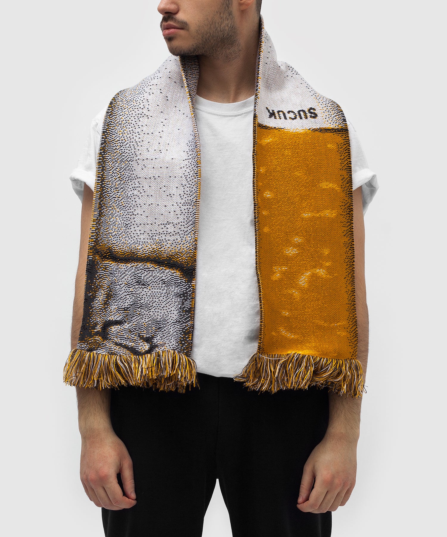 Person wearing a woven scarf designed to resemble a cigarette, featuring a detailed texture with an ash-like gray tip, a white middle section, and a golden-brown filter area. The scarf includes fringes on both ends and has the word “SUCUK” woven near the top.