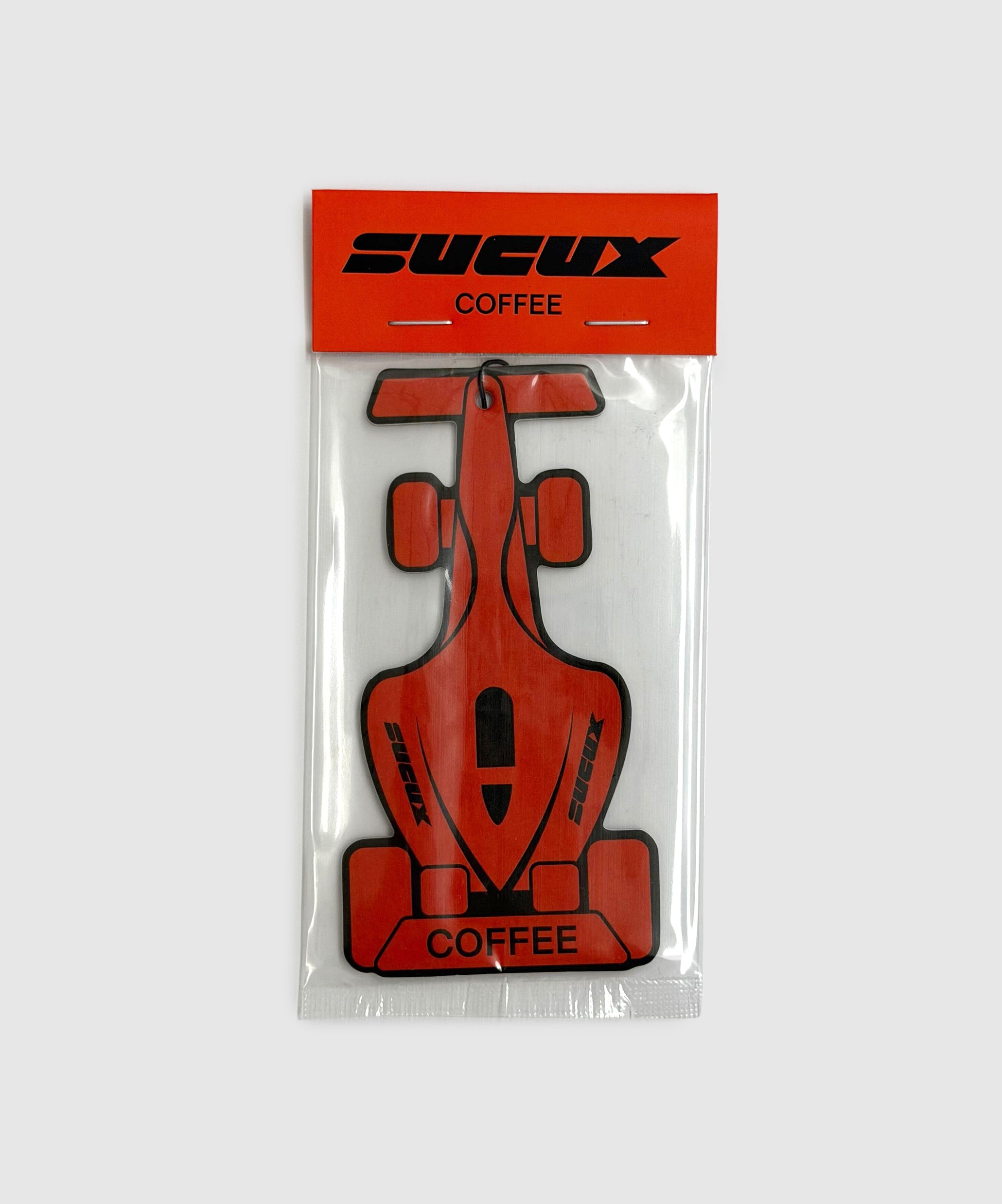 Orange Formula 1–shaped air freshener with black “SUCUX COFFEE” branding, packaged in a clear plastic sleeve with an orange header card.