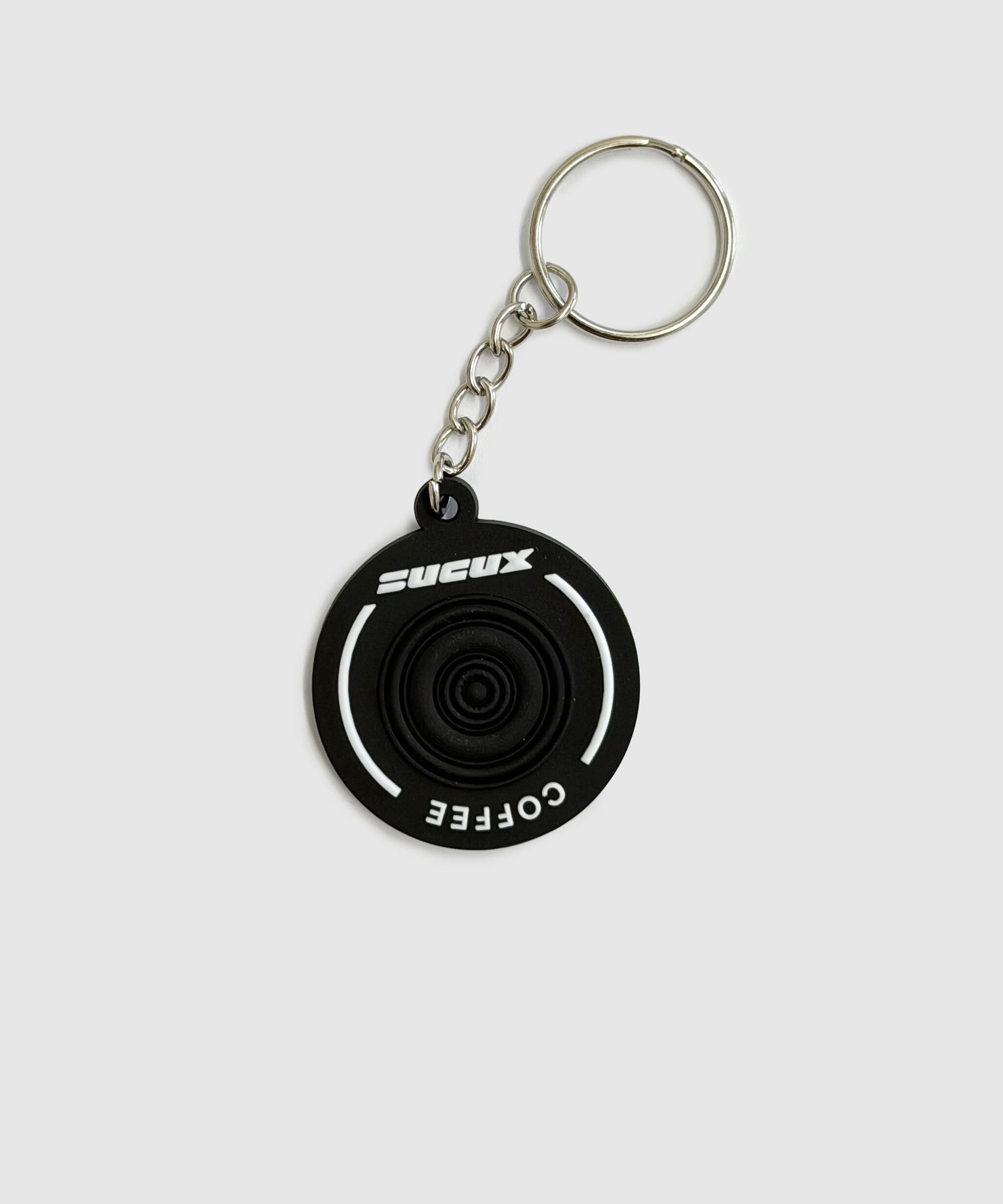 Black rubber keychain with circular design, featuring white “SUCUX COFFEE” branding and a metal key ring